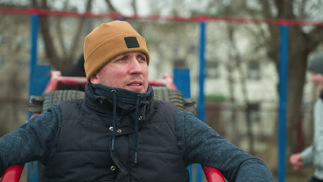 a focused coach sits on workout equipment, looking intent, in the background, two boys are seen playing football happily