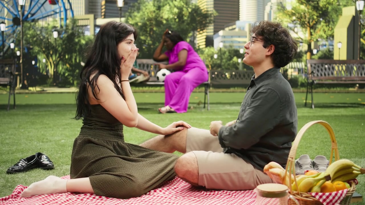 Expressive man gestures with both hands talking to woman seated on blanket