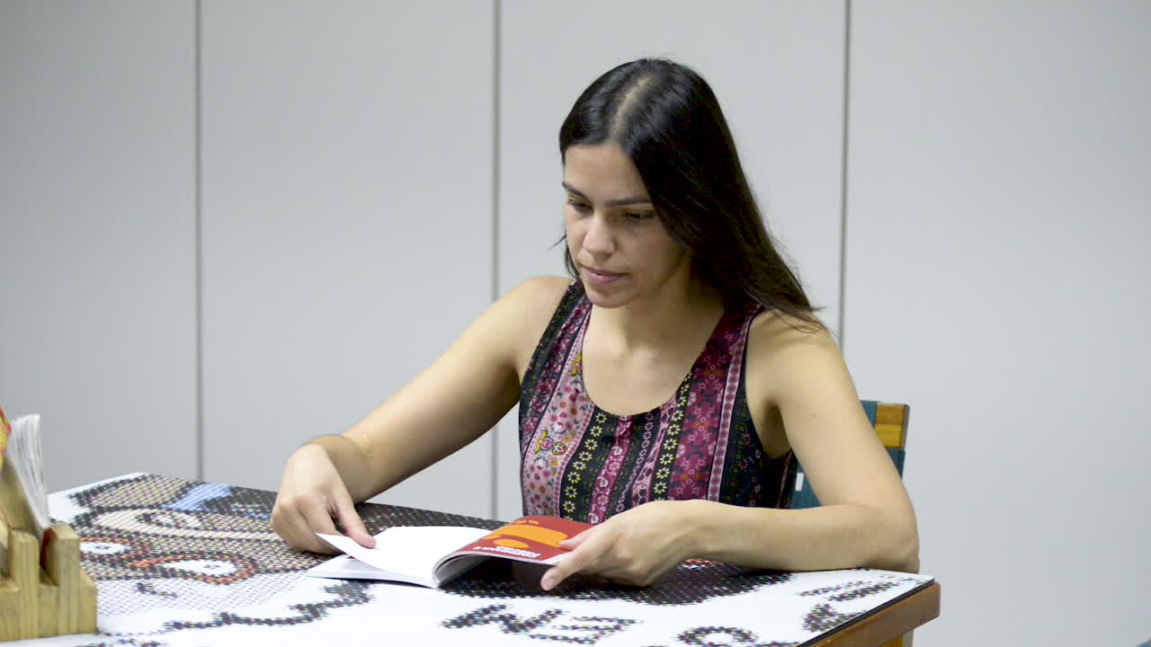 mujer morena bastante joven disfrutando de leer un libro sentado en la mesa