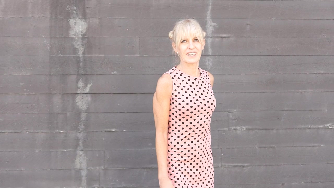 A confident woman in a polka dot dress with a modern touch strolls through the cityscape