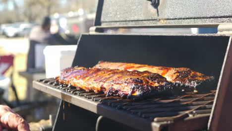 a man pouring bbq sauce on to a rack of ribs and placing them in a smoker