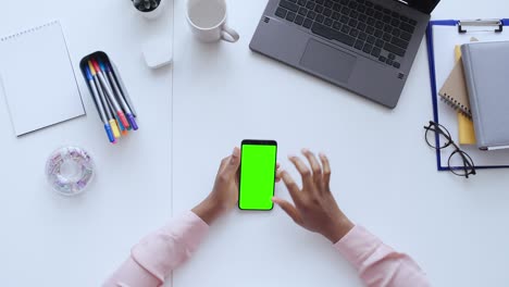 top view of female hands scrolling smartphone with green screen, business app