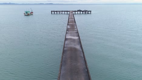 Drone-shot-of-a-pier-leading-into-the-sea-with-a-man-walking-on-it