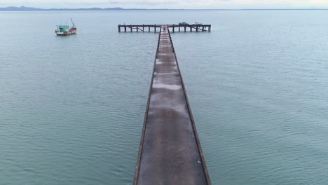 toma de drone de un muelle que conduce al mar con un hombre caminando sobre él.