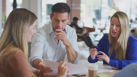 business team having meeting sitting around table discussing document in modern open plan office