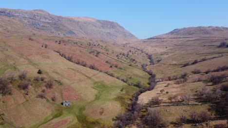 vista inversa de drones del piso del valle del área del paso de kirkstone mirando hacia los pedregales rojos cayeron con el antiguo edificio de la granja y los colores otoñales