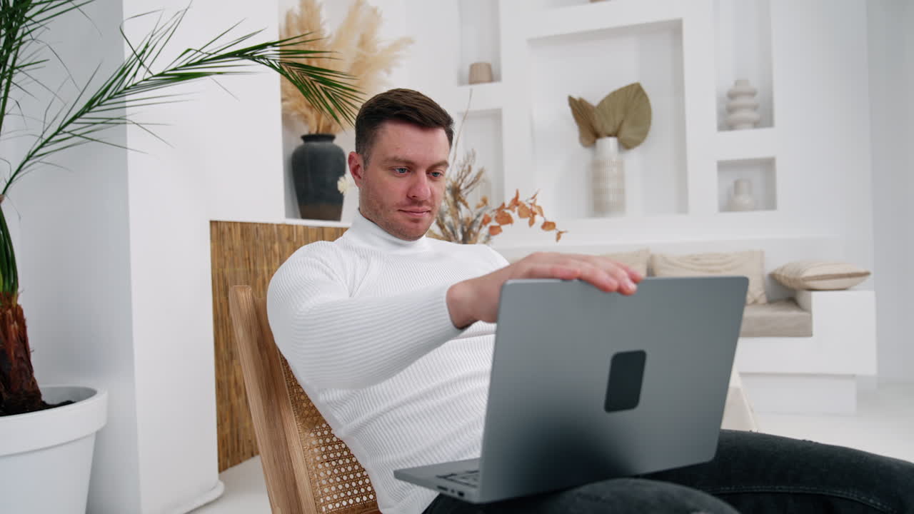 Attractive Caucasian male closes his laptop. Happy man leaning in the armchair relaxed after work.
