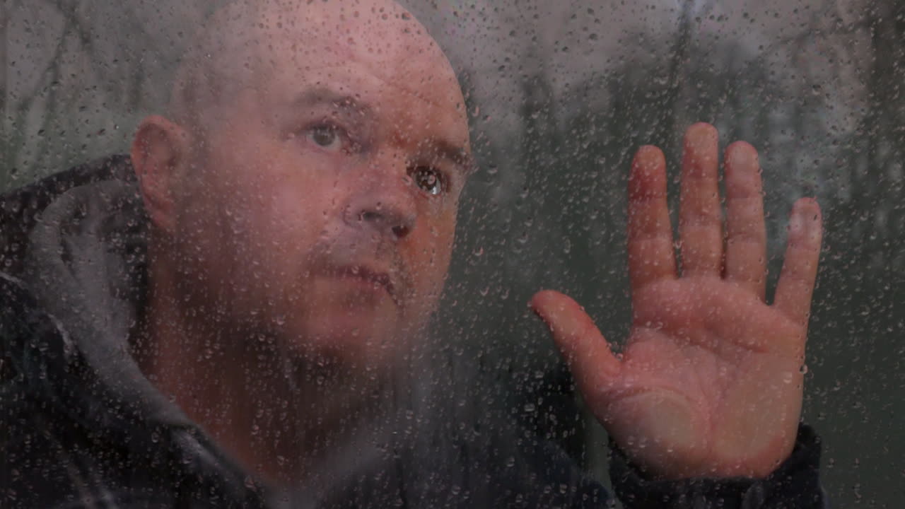 창문을 통해 폭풍 구름과 비를 바라보며 고립된 생각에 잠겨있는 남자