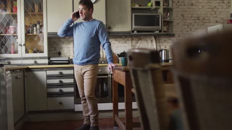 Caucasian-man-using-smartphone-and-talking-in-kitchen-at-home