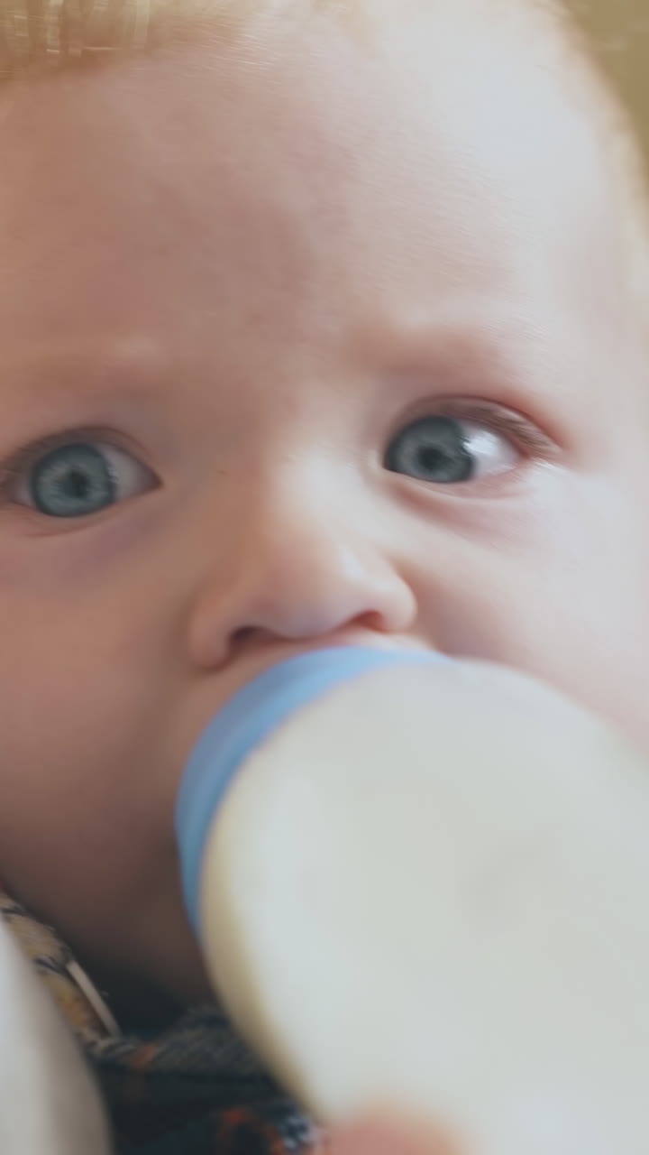 careful mother feeds little tired baby with tasty milk mix from bottle in light room extreme close view