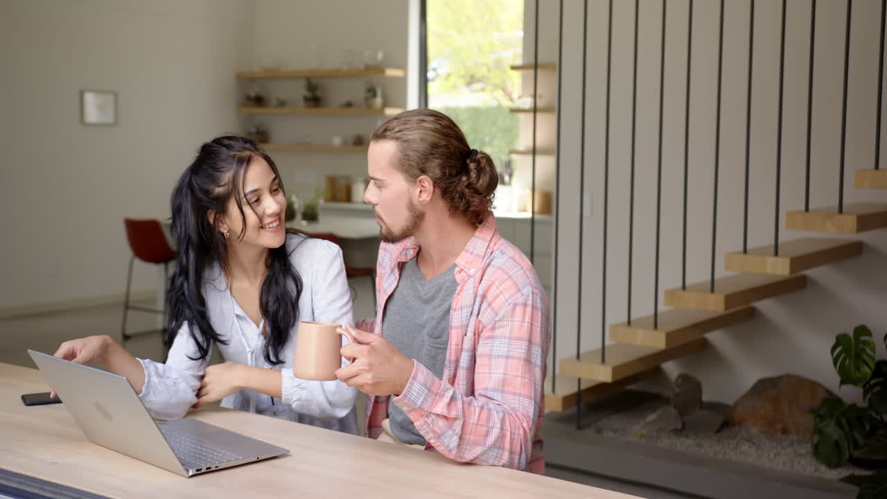 Young happy couple are looking at laptop together, in kitchen at home