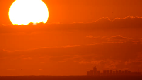 Un-Carguero-Viaja-A-Lo-Lejos-A-Través-Del-Horizonte-Del-Océano-Bajo-Un-Enorme-Sol-Naciente,-Iluminando-El-Cielo-De-Color-Naranja-Brillante