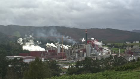 Zeitraffer-Einer-Papierindustrie-Mit-Vielen-Schornsteinen,-Die-An-Einem-Bewölkten-Und-Windigen-Tag-Rauch-Ausstoßen-Und-Die-Umwelt-In-Einer-Grünen-Ländlichen-Gegend-Verschmutzen