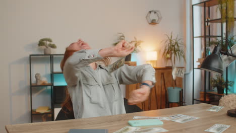 successful woman freelancer using smartphone celebrate success falling money at home office desk
