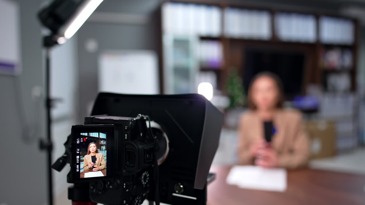 Brunette Caucasian woman talks on the display of camera on tripod. Blurred backdrop. Blog content creation.
