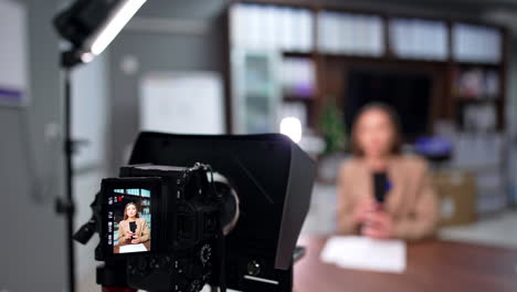 brunette caucasian woman talks on the display of camera on tripod. blurred backdrop. blog content creation.