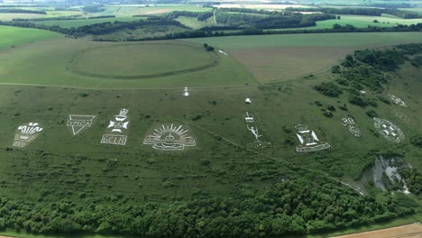 Fovant-military-badges-carved-into-the-Wiltshire-chalk-hill-Orbiting-aerial-view-across-green-English-countryside-landmark