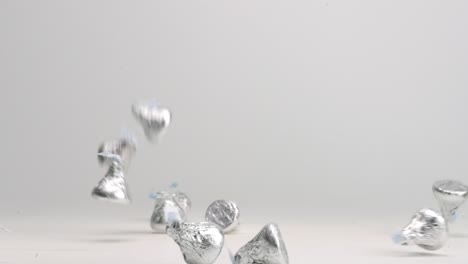 silver wrapped chocolate hershey candies bouncing into pile on white table top in slow motion