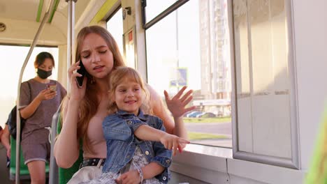 young family woman with kid girl sitting in public bus transport, mother talking on mobile phone