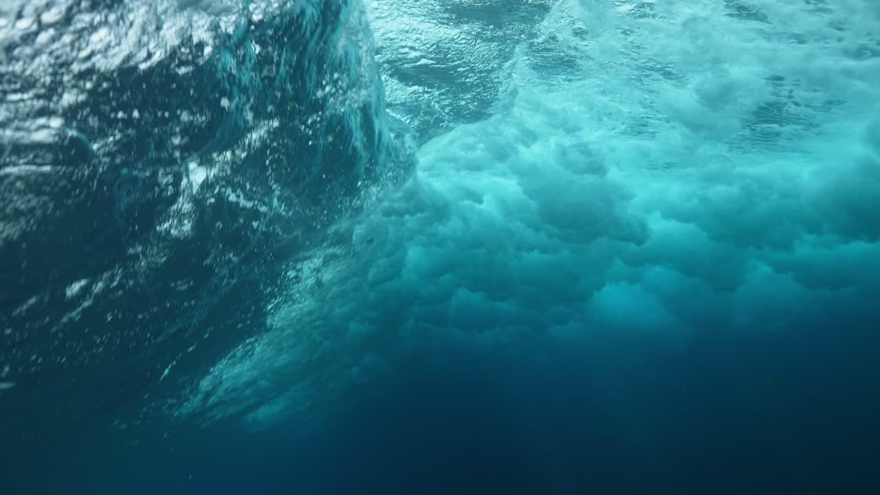 View of powerful ocean wave from below, water swirling with foam and energy in deep blue sea
