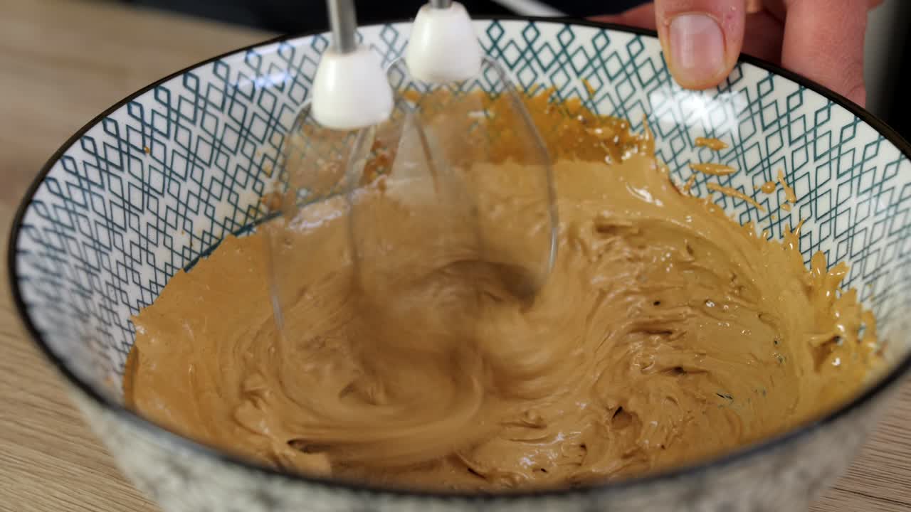 Woman uses electric handheld mixer to whip dalgona coffee whipped cream, closeup