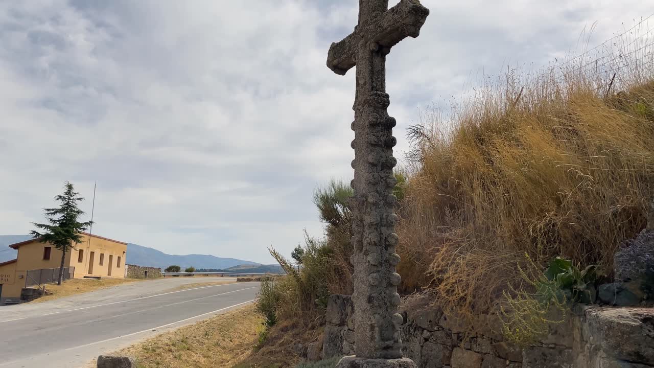 Slow motion footage of a Gothic stone cross placed at a road junction to indicate the proximity of a shrine. The numerous balls that form the cross draw our attention.