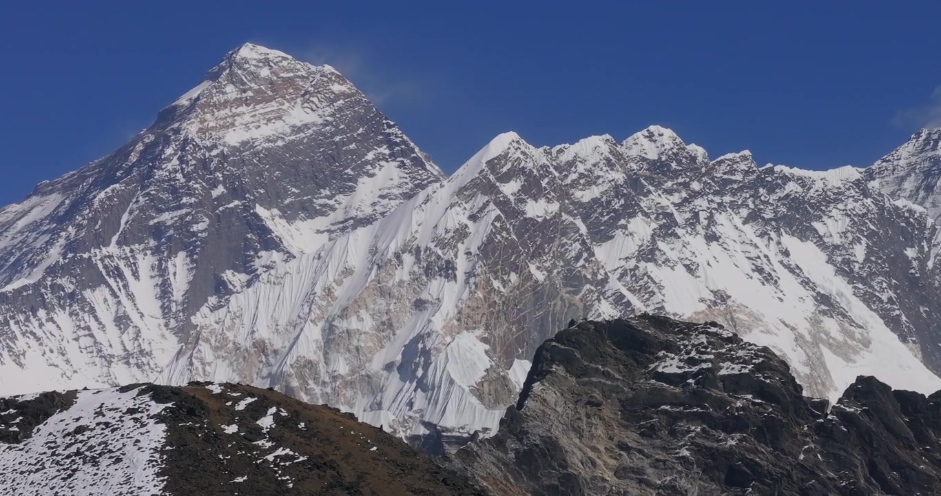 Gokyo Ri, Nepal, ripresa con drone che mostra l'iconica vetta innevata del Monte Everest accanto alle imponenti catene himalayane contro un cielo azzurro limpido.