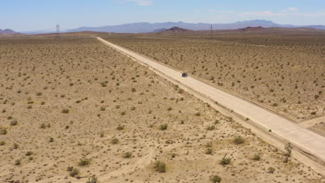 large black suv speeds down a straight dirt desert road leaving a dust cloud behind