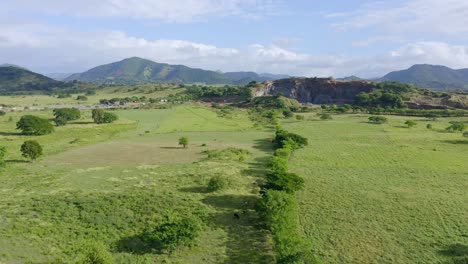 aerial forward over green fields surrounding open pit volcanic rock mine