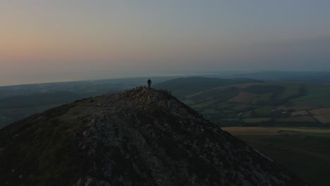 Aerial---Flying-from-front-to-behind-the-man-standing-on-top-of-the-mountain-watching-beautiful-sunset-sunrise-over-the-peaks