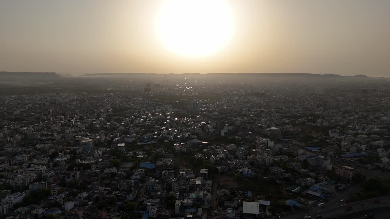 High-altitude aerial view showcasing the dense urban sprawl of Jaipur, the Pink City, with iconic architecture and bustling streets during sunset.