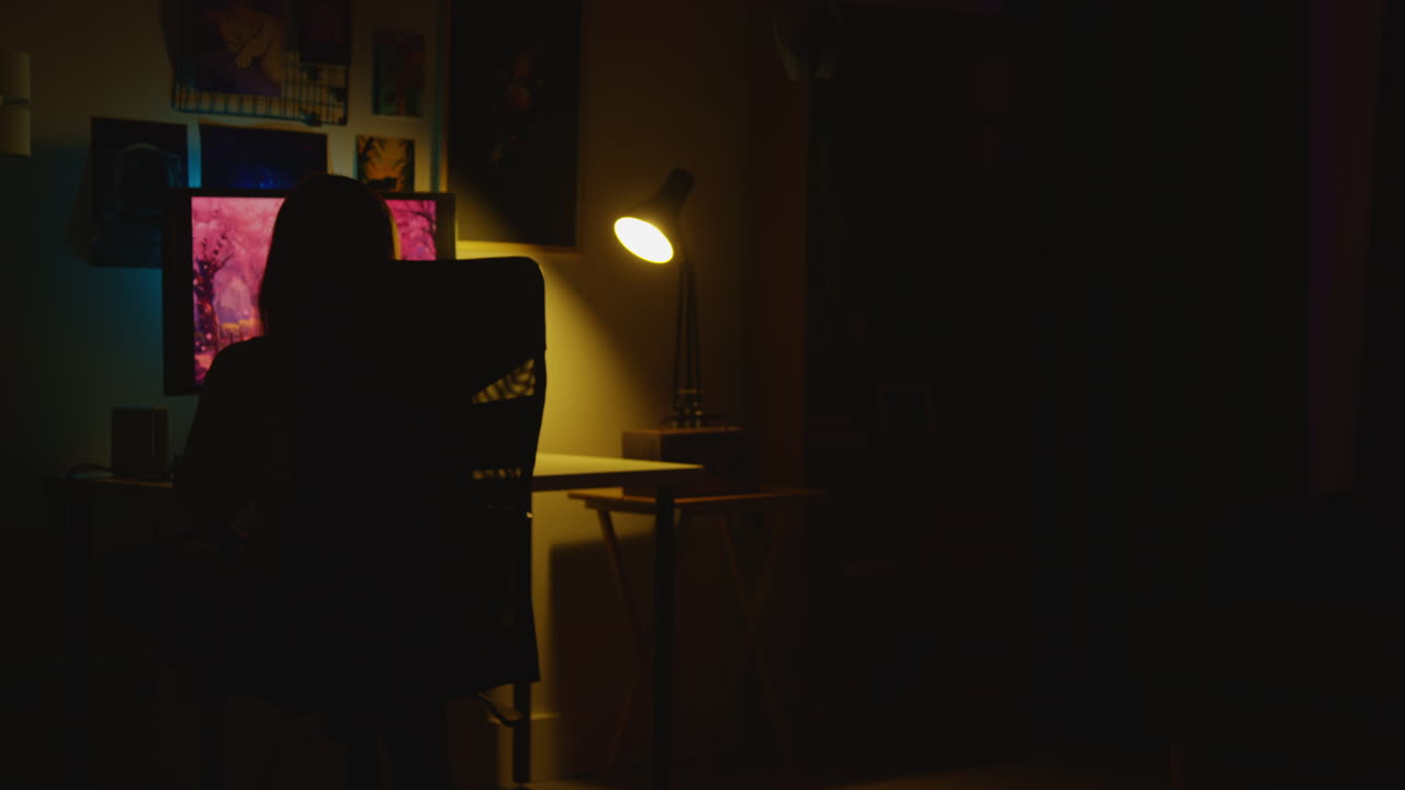 컴퓨터 를 사용 하는 어두운 방 에서 책상 에 앉아 있는 사람