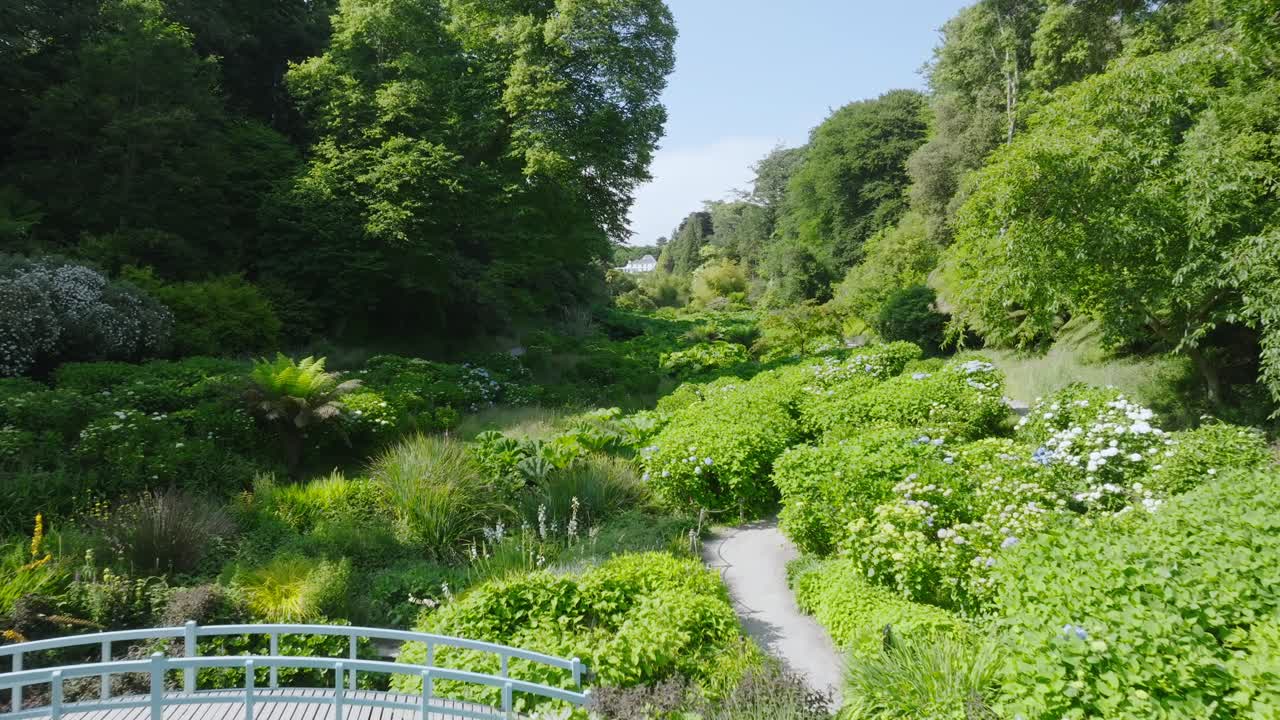 Small white wooden bridge with pathway in tropical garden tree lined valley with white mansion at the valley head.