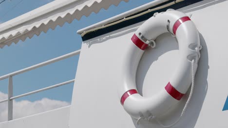 rescue ring with red warning colors on white ship railing in front of blue sky in the daytime without people