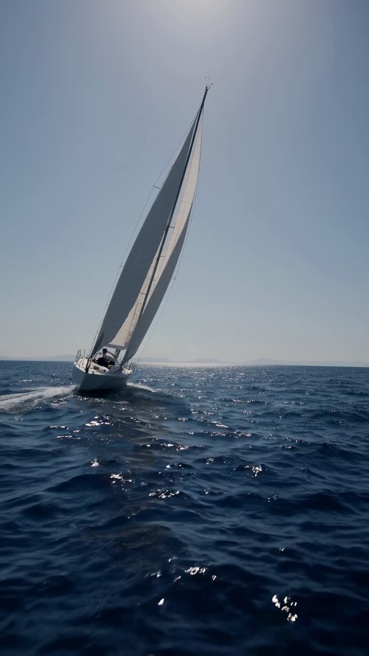 Un'inquadratura dinamica dal basso di una barca a vela che scivola attraverso acque blu scintillanti sotto un cielo sereno.