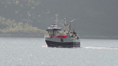 fishing trawler sailing along husoya island, nordland, norway