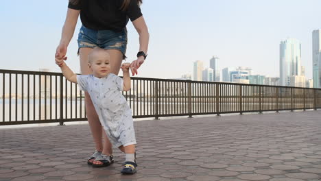 the boy holding his mother's hand makes the first steps walking along the promenade in the summer