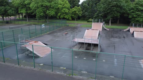 Aerial-view-flying-rising-above-fenced-skate-park-ramp-and-tennis-court-in-empty-closed-playground