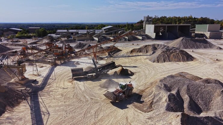 Heavy machinery operates at a gravel site in bright daylight