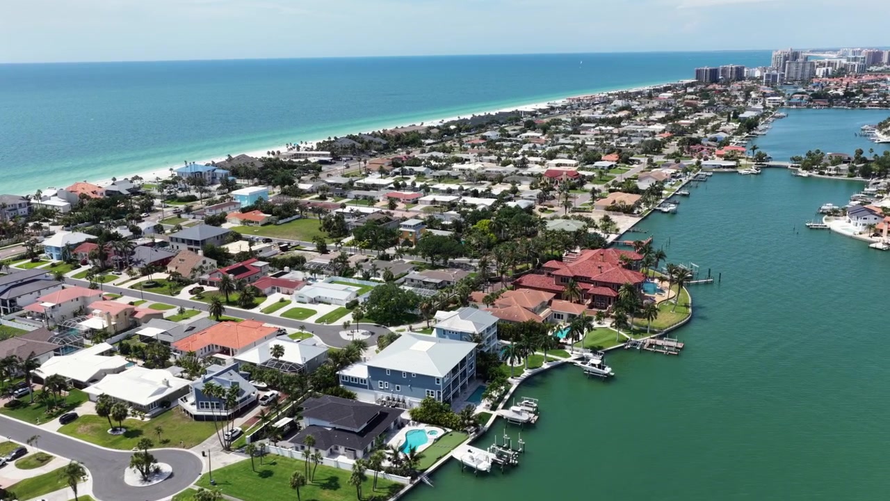 L'isola barriera di Clearwater Beach si estende tra la costa turchese del Golfo e la via navigabile interna, con case di lusso, moli, piscine e lo skyline sullo sfondo. Florida, USA. Ripresa aerea con drone.