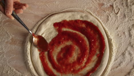 pizza chef putting ketchup tomato sauce on raw dough in kitchen restaurant.