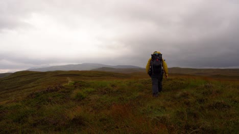 an einem launischen tag über schottisches moorland durch heide in richtung hügel wandern