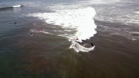 Aerial-following-shot-shows-a-guy-surfing-a-wave-dodging-some-other-surfers-having-fun-on-the-beach