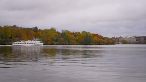 a white small ferry is going from one island to another in stockholm in the autumn with colorful trees