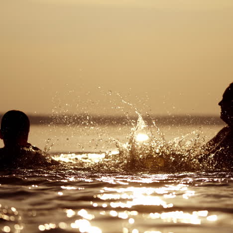 Silhouette of a boy in lake with many drops of water on him. Splashing of water on a boy in the river. Mother and her children enjoying the time together in water at sunset.