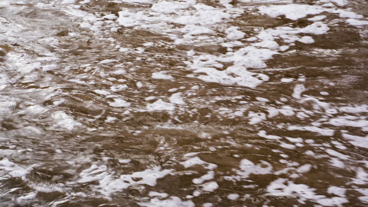 Muddy bubbling river water with strong current, closeup on surface
