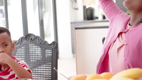 African-american-brother-and-sister-eating-breakfast-at-table-in-kitchen,-slow-motion