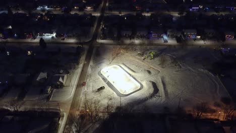 illuminated outdoor skating rink in a snowy park at night in st constant, quebec, canada. pull back shot