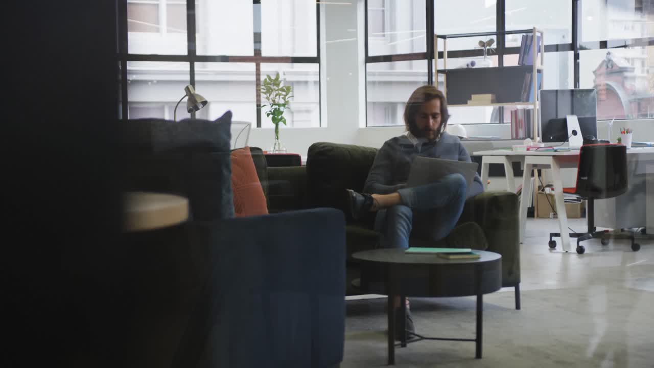 Kaukasisk forretningsmann som sitter på sofaen og bruker en bærbar datamaskin på et moderne kontor.