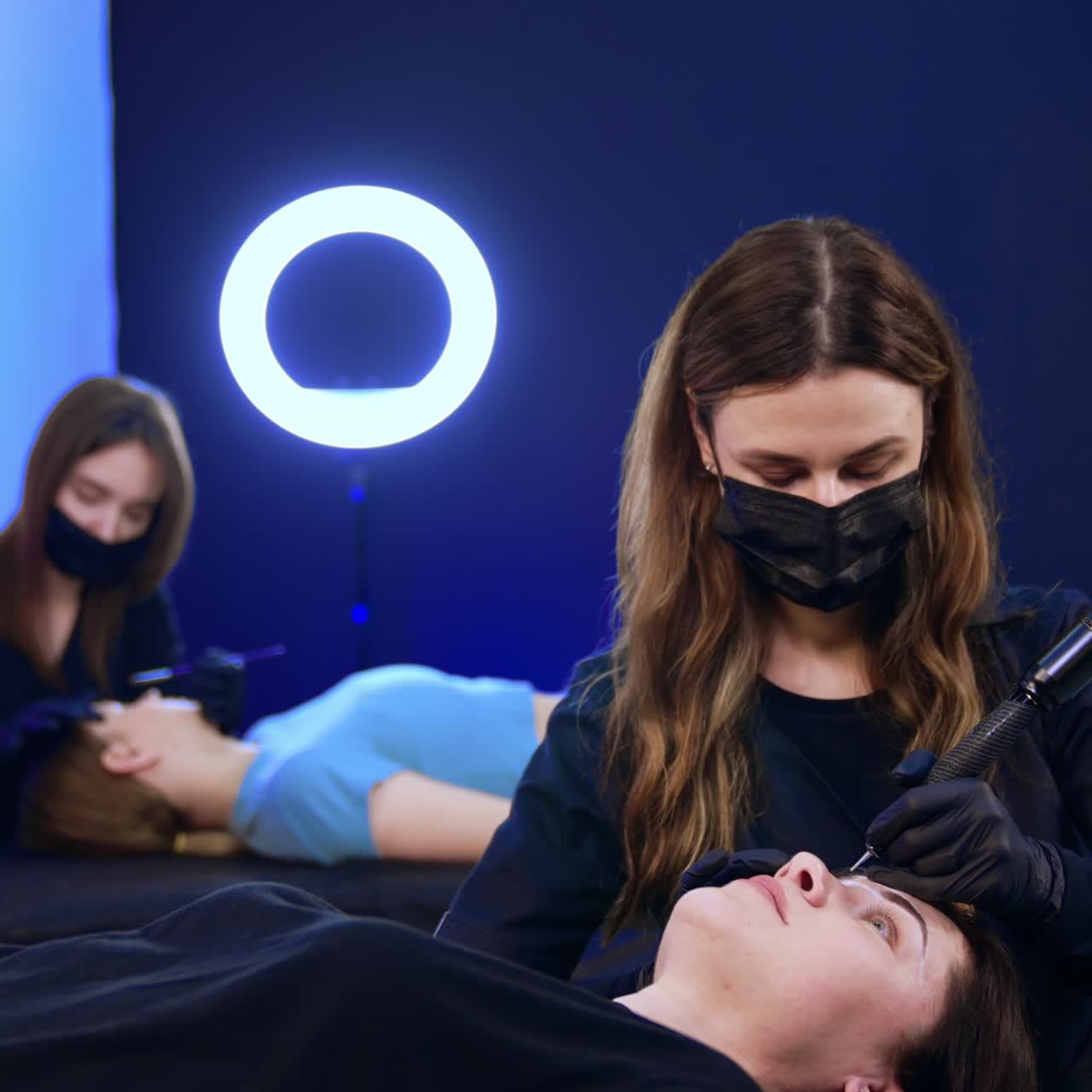 Salon brow masters performing permanent brow make up to the clients. Beauty professionals work in masks
